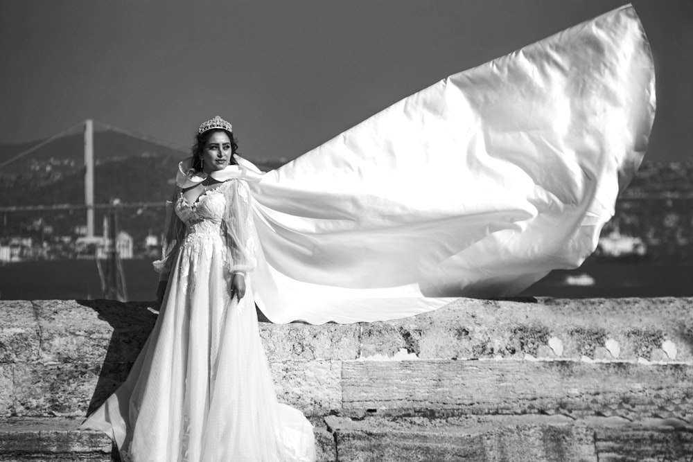 grayscale photo of woman in white dress standing on concrete wall