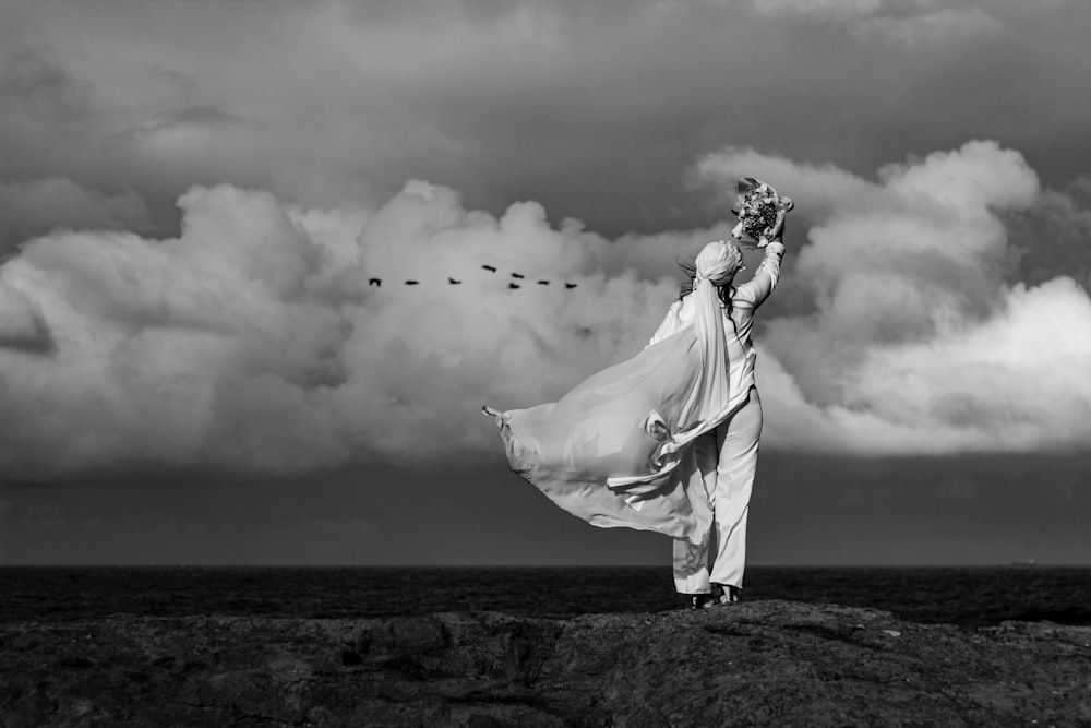 woman in white dress standing on black sand under cloudy sky during daytime