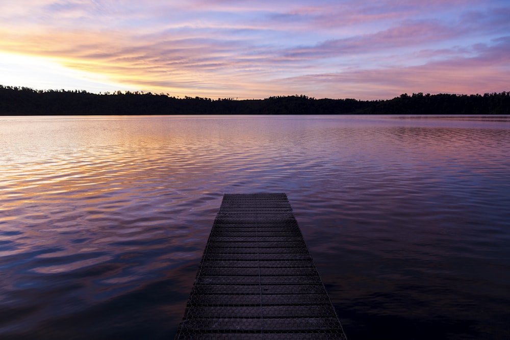 brown wooden dock on lake during sunset