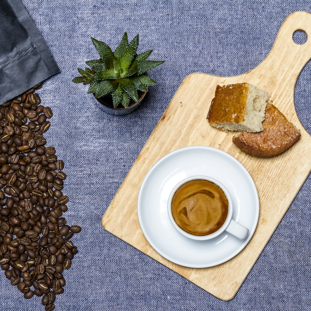 white ceramic cup on white ceramic saucer beside brown wooden chopping board