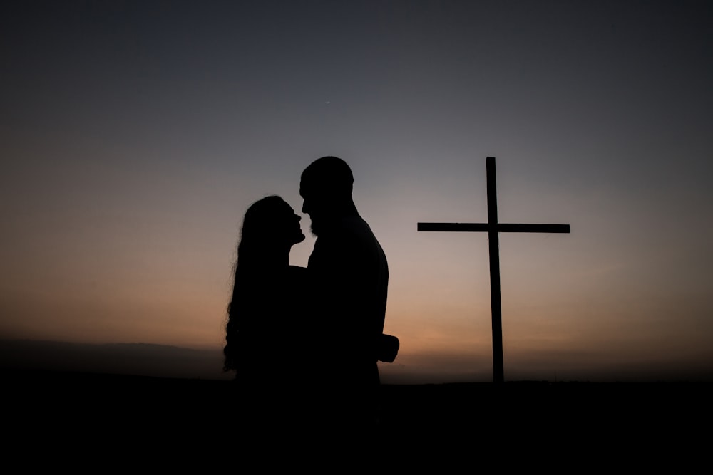 夕暮れ時の十字架の脇に立つ男女のシルエット