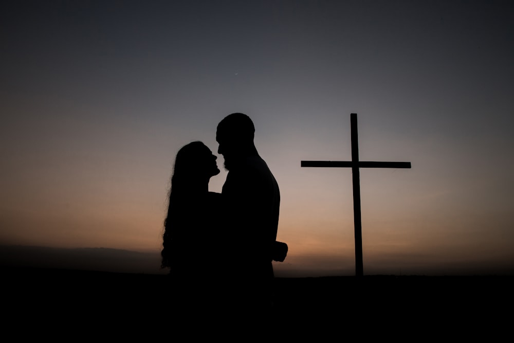 Silhouette d’homme et de femme debout à côté de la croix pendant le coucher du soleil