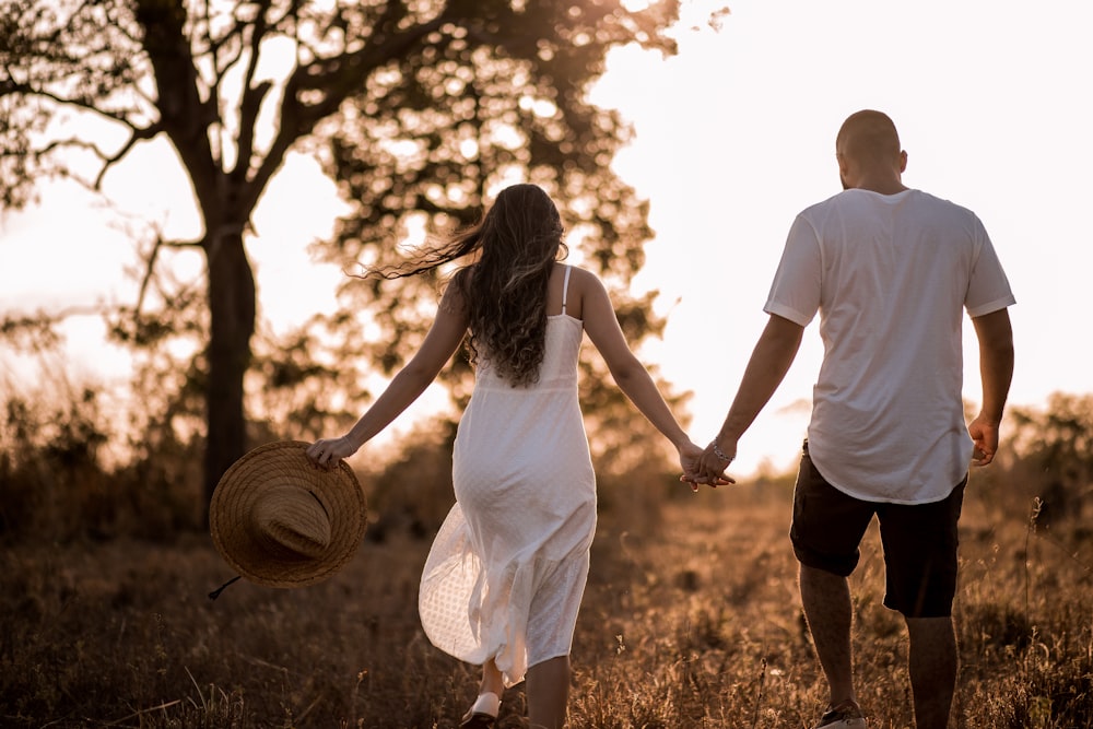 homme et femme se tenant la main tout en marchant sur un champ d’herbe pendant la journée