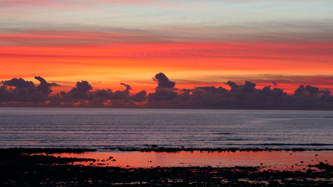 silhouette of man sitting on rock formation near body of water during sunset