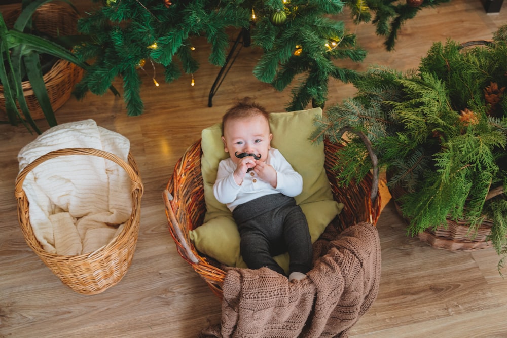 baby in white shirt and gray pants sitting on brown wicker armchair