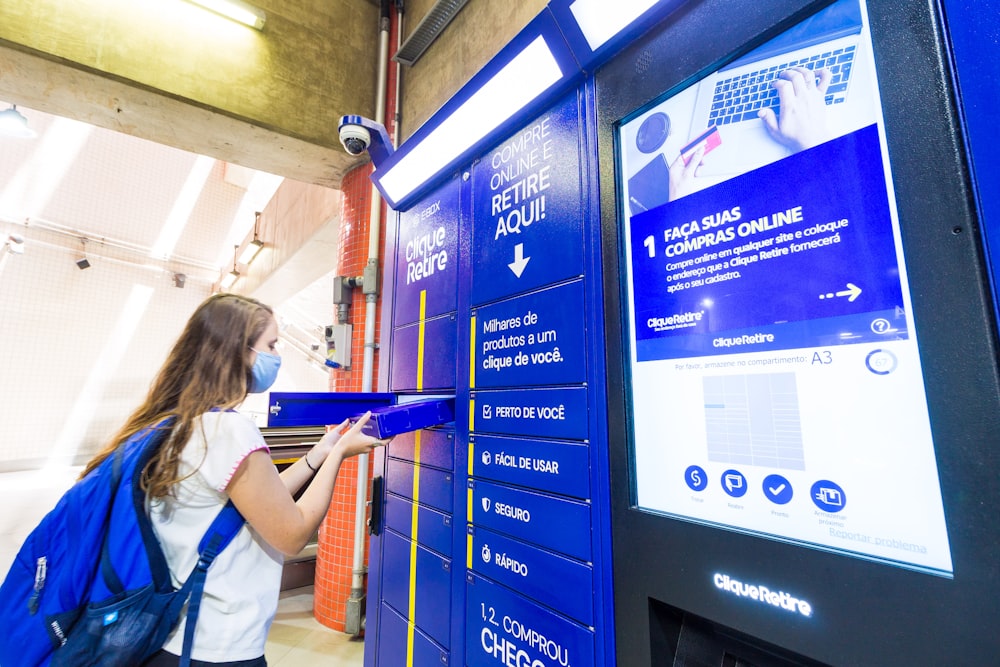 woman in white t-shirt standing beside blue and red vending machine