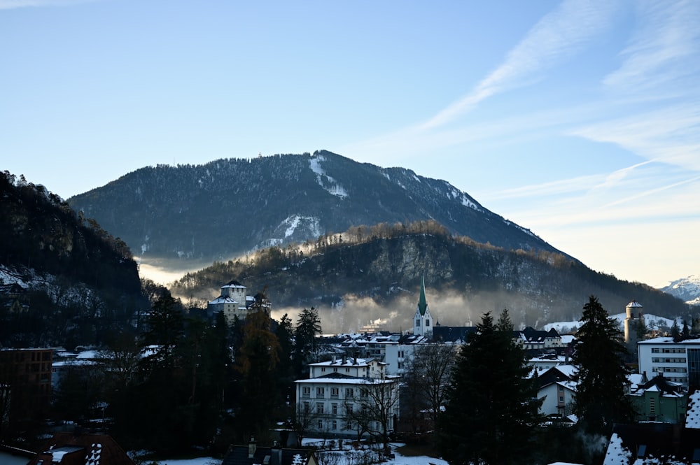 white and black concrete building near green trees and mountain under blue sky during daytime