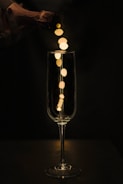 A champagne bottle is being poured into a tall, elegant glass with bokeh lights cascading from the bottle neck into the glass. The background is dark, highlighting the golden reflections and the sleek form of the glass.