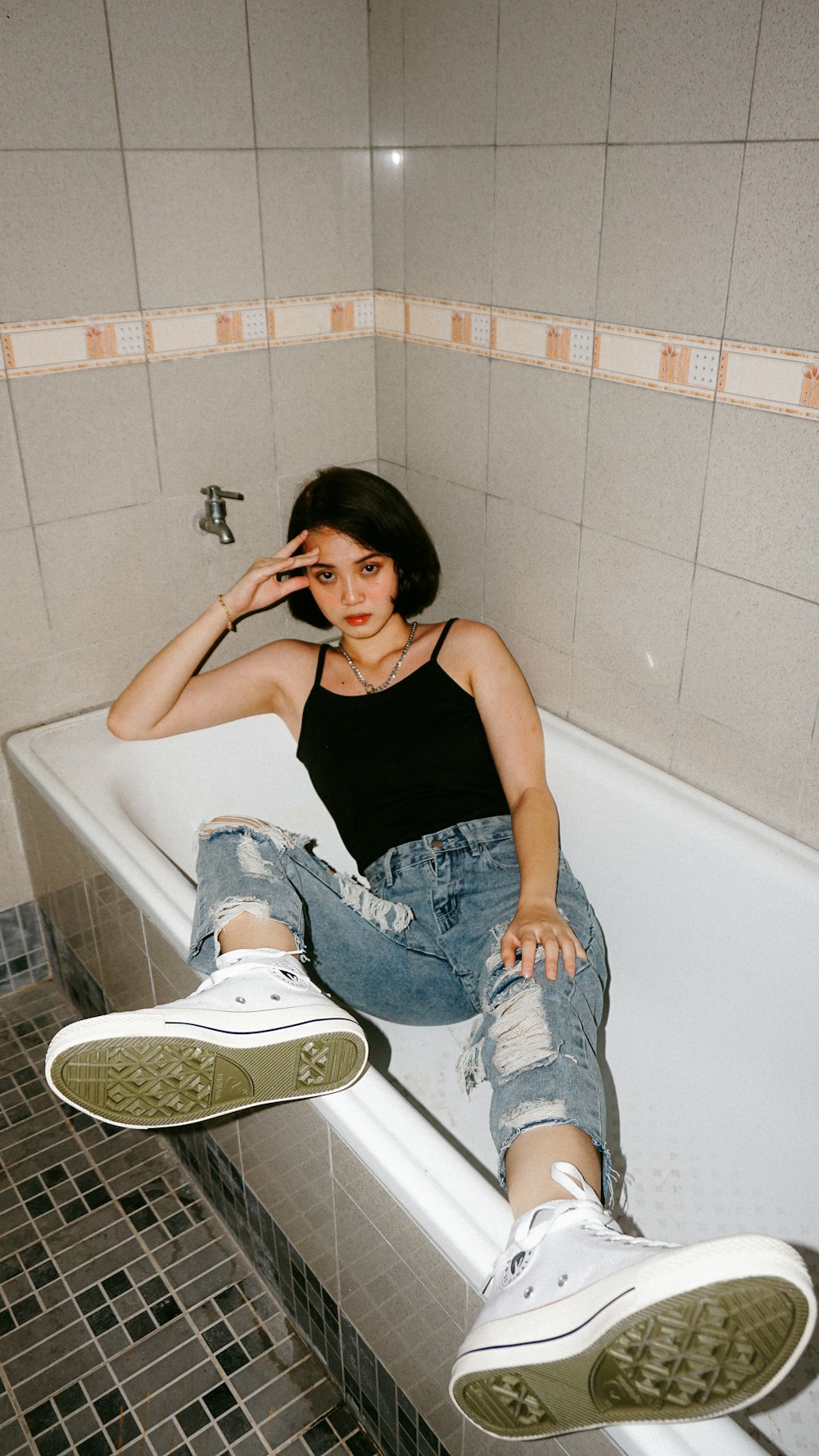 Frau in schwarzem Tanktop und blauer Jeans sitzt auf der Badewanne