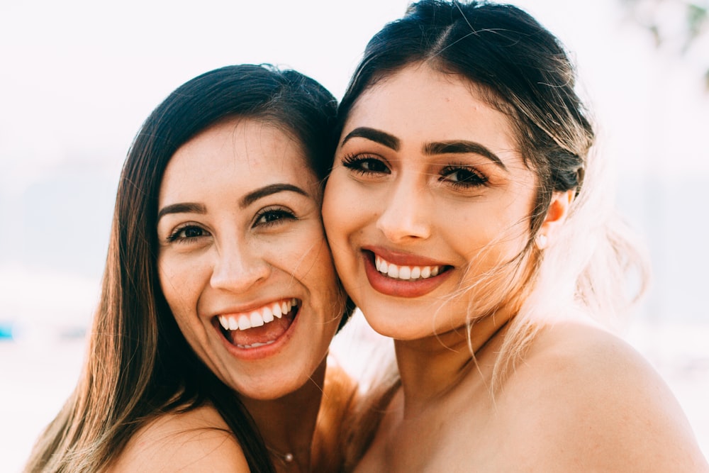 2 smiling women smiling in front of white background
