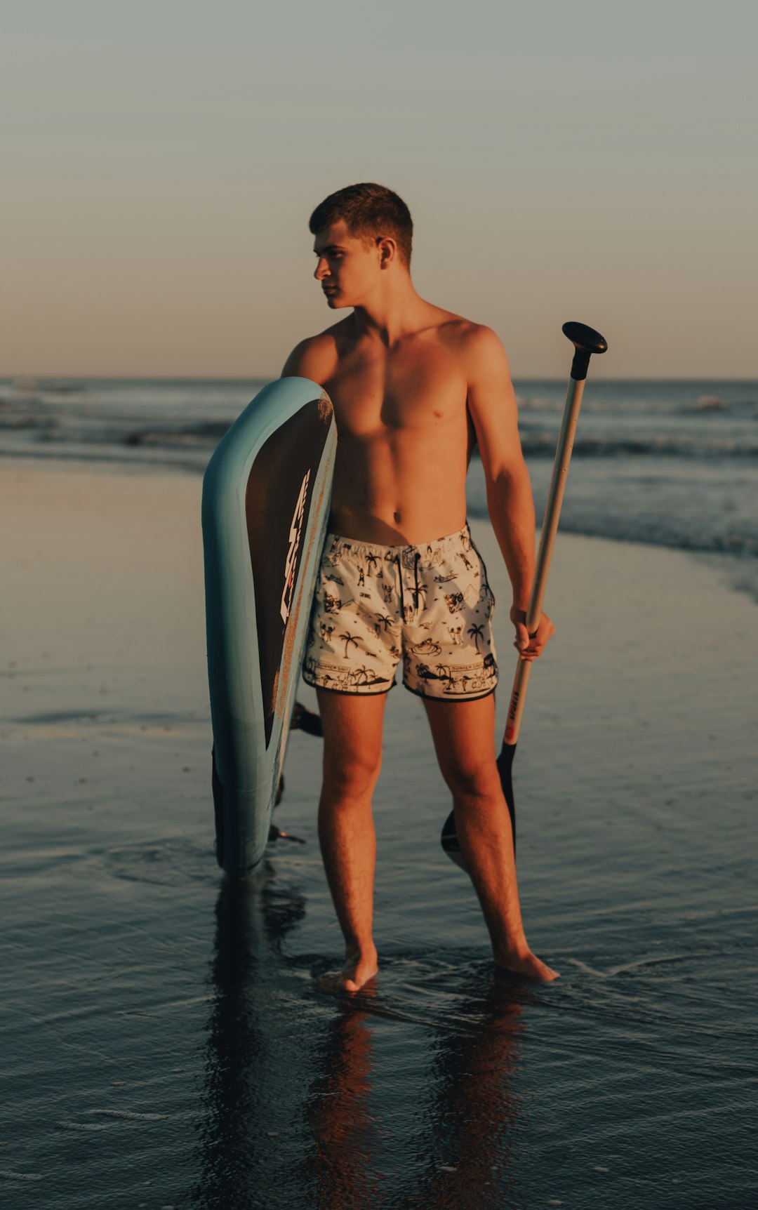 topless man in white and black shorts holding brown wooden stick standing on beach during daytime