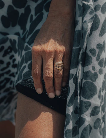 A stylish hand wearing a simple, bright ring against a softly lit, neutral backdrop.