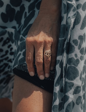 A hand wearing a minimalist black and deep red-brown ring, resting gently on a textured fabric.