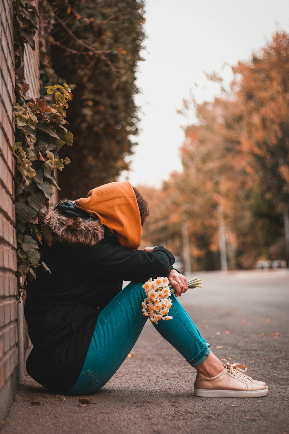 woman in brown and black jacket and blue pants sitting on gray concrete road during daytime