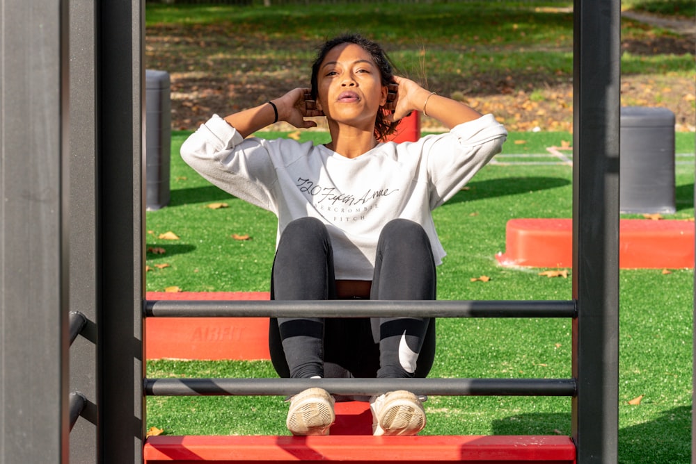 mulher na camisa branca da manga comprida e calças pretas sentadas na armação vermelha do metal