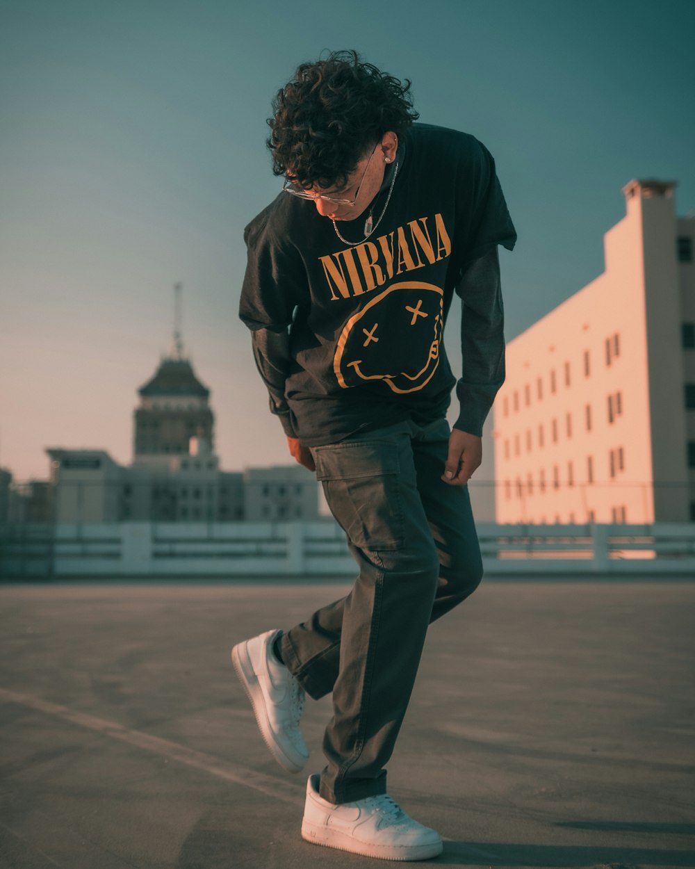 man in black and brown hoodie and black pants walking on gray concrete pavement during daytime