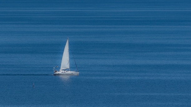 A sleek sailboat gliding on calm blue waters under a clear sky.