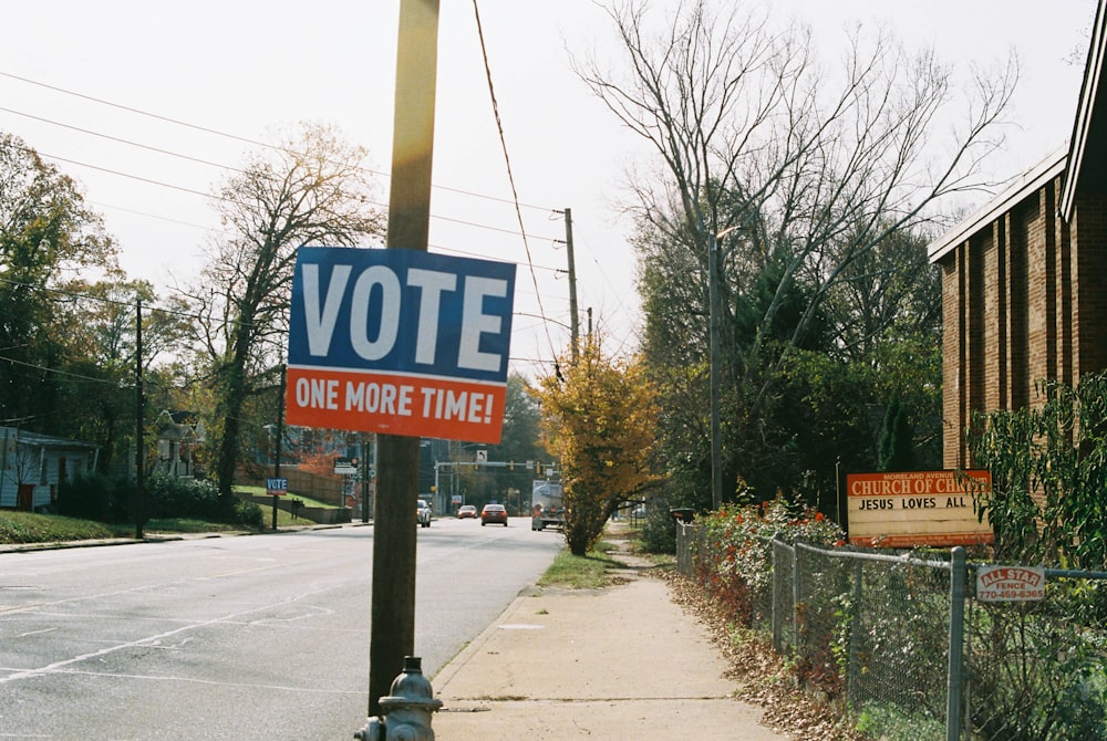 a vote sign on a pole next to a street