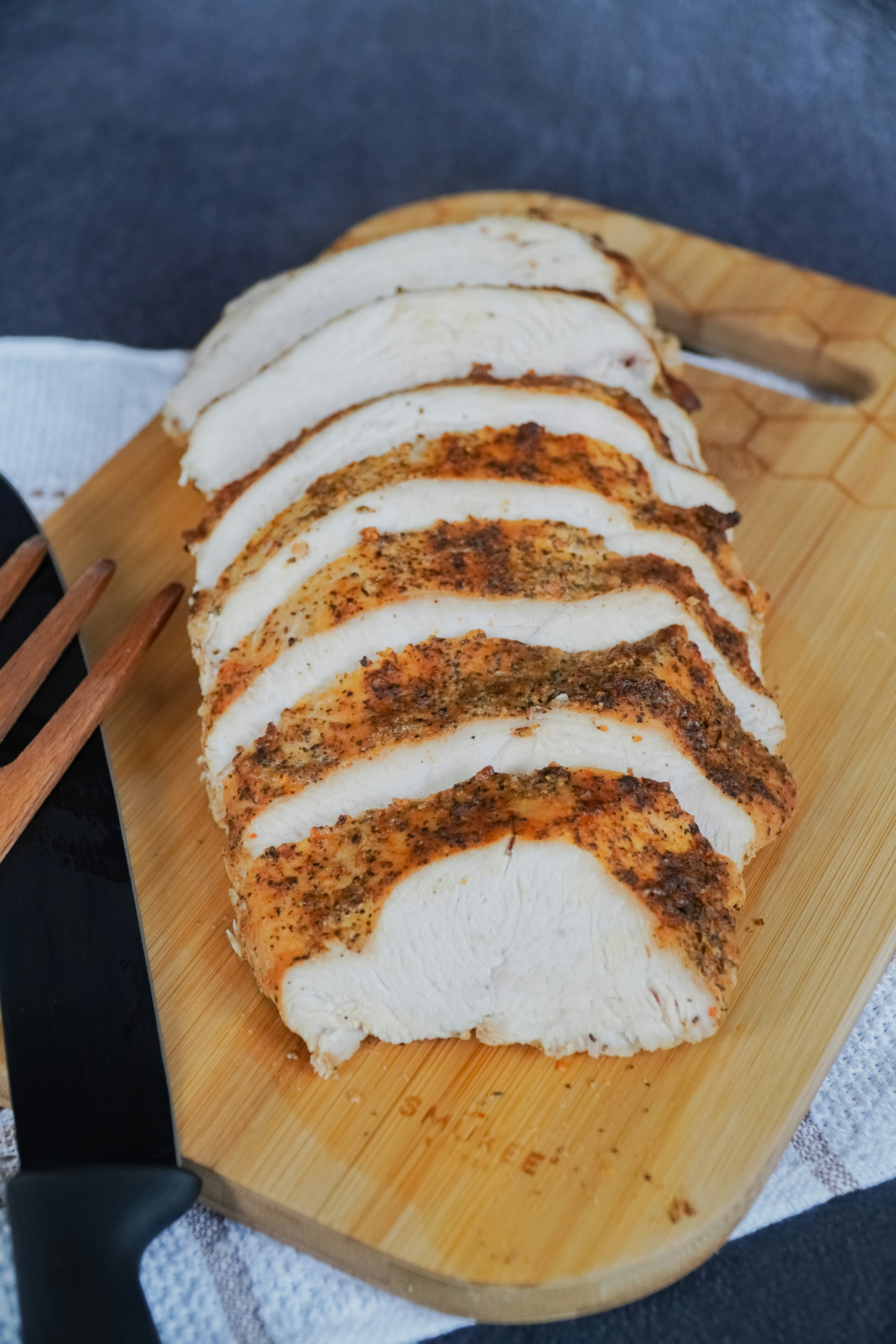Sliced chicken breast with golden-brown seasoned crust on wooden board`