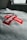 A close-up view of a gray sweatshirt featuring a red logo with white text in a cross shape, placed prominently on the fabric. The background shows a window with some light coming through, creating a soft, natural lighting effect on the garment.