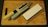 A kitchen knife with a beige handle rests on a sharpening stone, next to a whetstone on a wooden cutting board. The knife has multiple cutout holes in the blade.