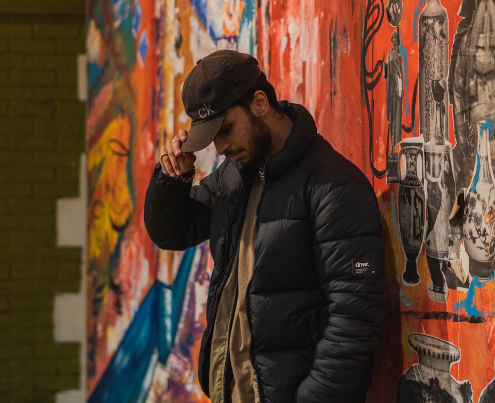 man in black jacket standing beside graffiti wall