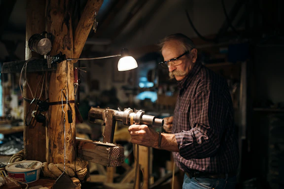 A craftsman’s hands shaping a wooden plank with traditional tools in a warmly lit workshop.