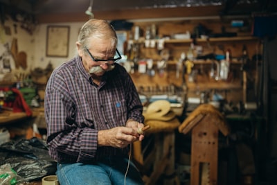 man in black and white plaid dress shirt and blue denim jeans sitting on brown wooden santa's workshop teams background