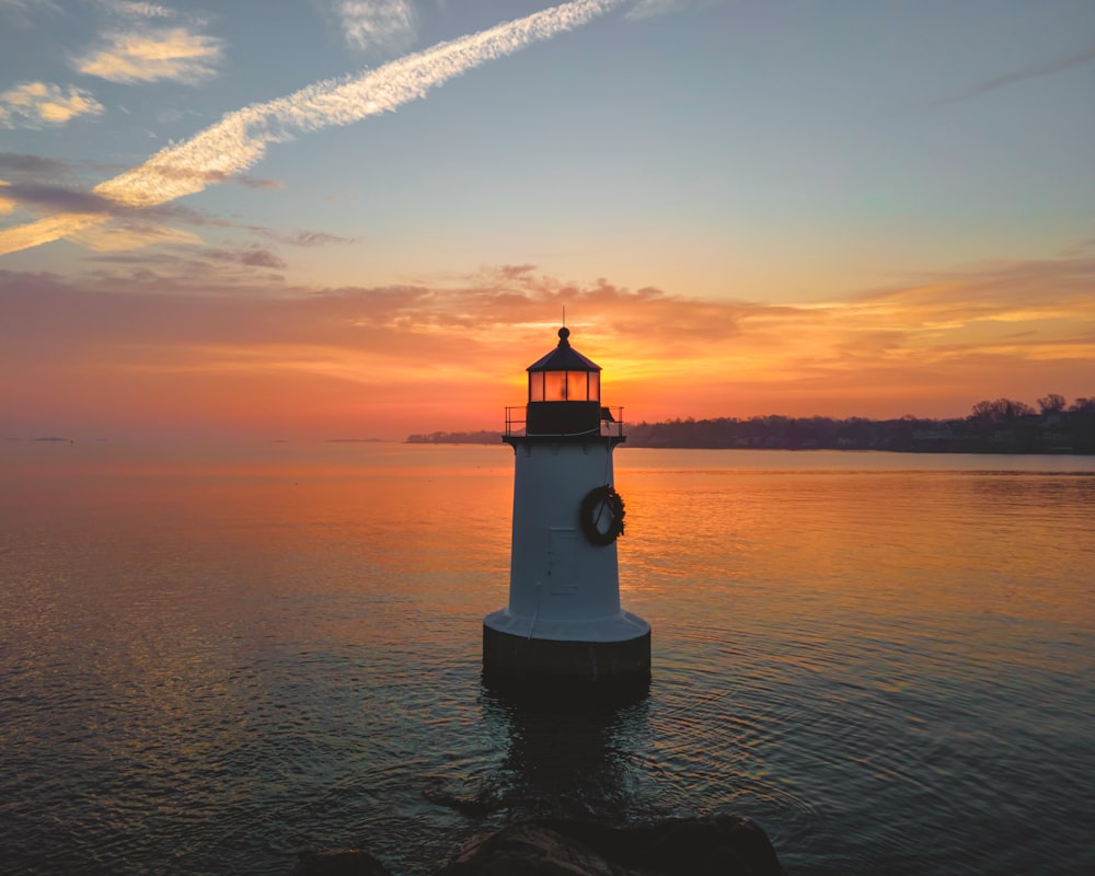 white and black lighthouse on body of water during sunset