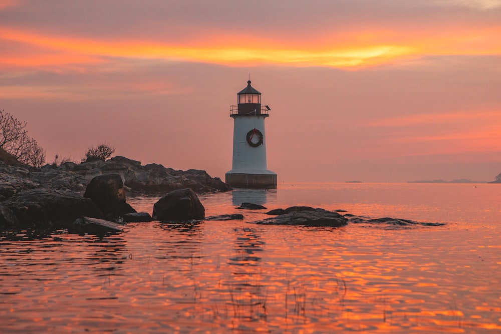 white lighthouse on rock formation on sea water during sunset