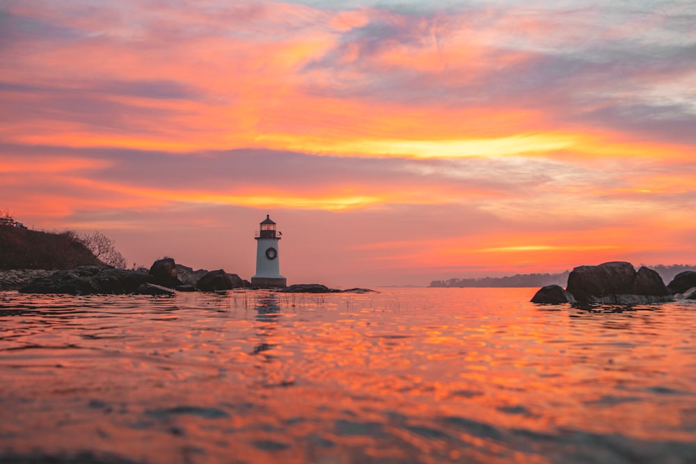 white and black lighthouse on beach during sunset