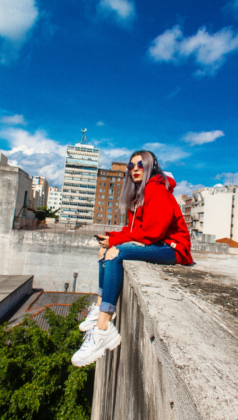 woman in red hoodie and blue denim jeans sitting on concrete bench during daytime