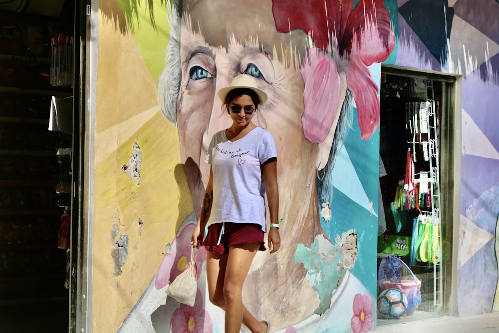 Mujer con camisa blanca y pantalones cortos negros de pie junto a la pared con graffiti