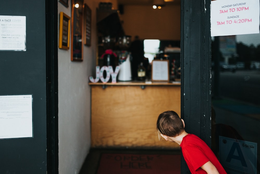 boy in red and white shirt standing near brown wooden door