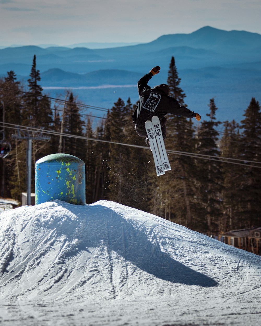 person in black jacket and blue pants riding on ski lift over snow covered mountain during