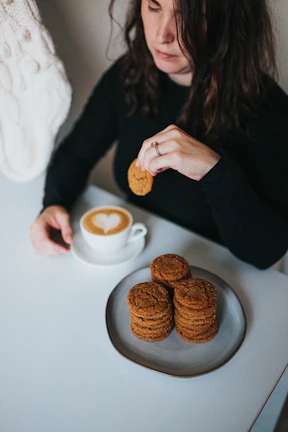 A happy customer enjoying a cookie with a warm cup of coffee by a window.