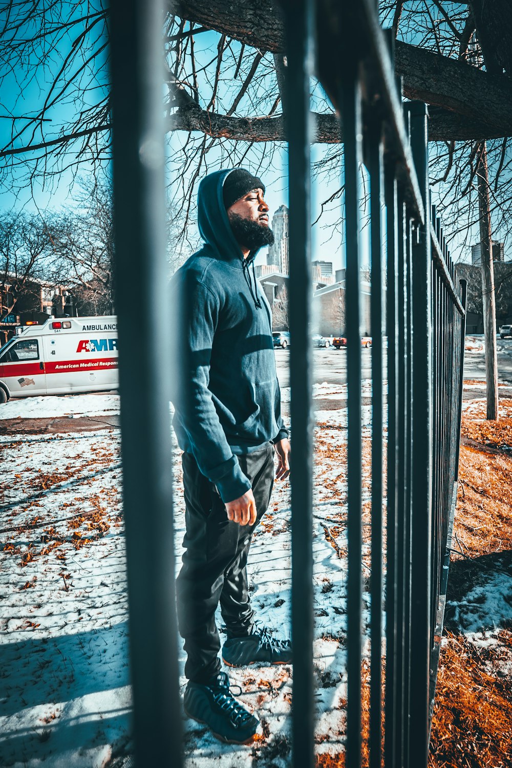 man in gray hoodie standing beside gray steel fence during daytime