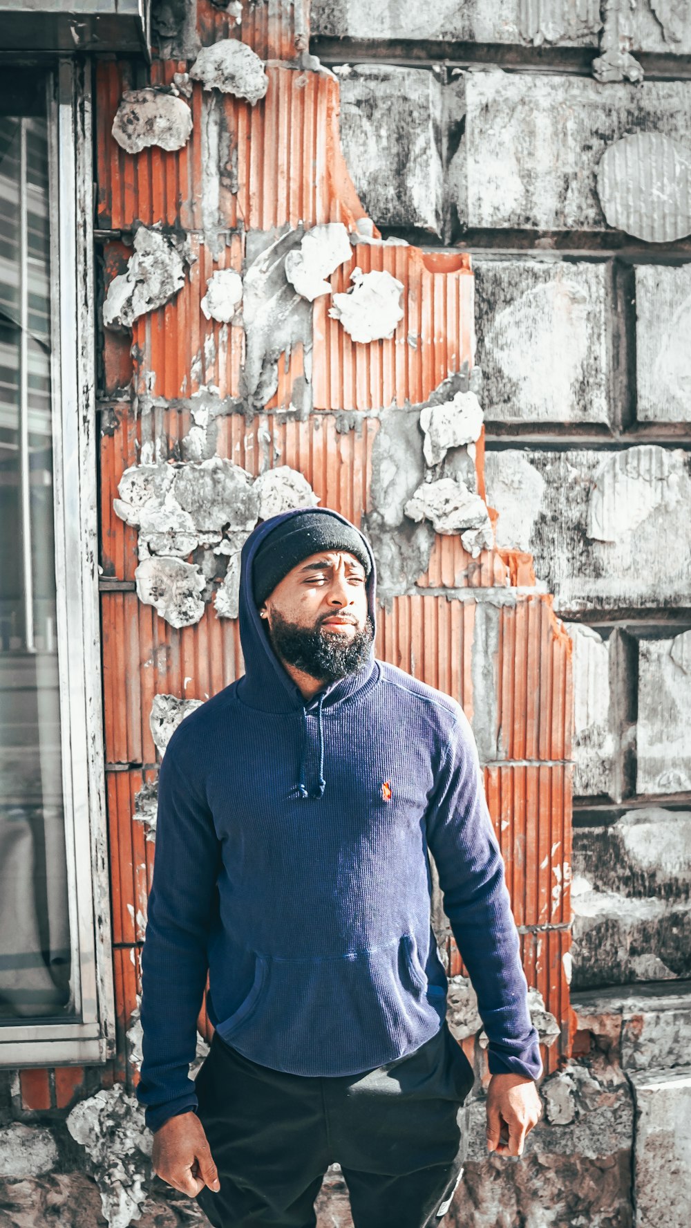 man in blue long sleeve shirt standing beside brown and white concrete wall