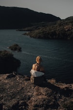 woman in white dress sitting on brown rock near body of water during daytime