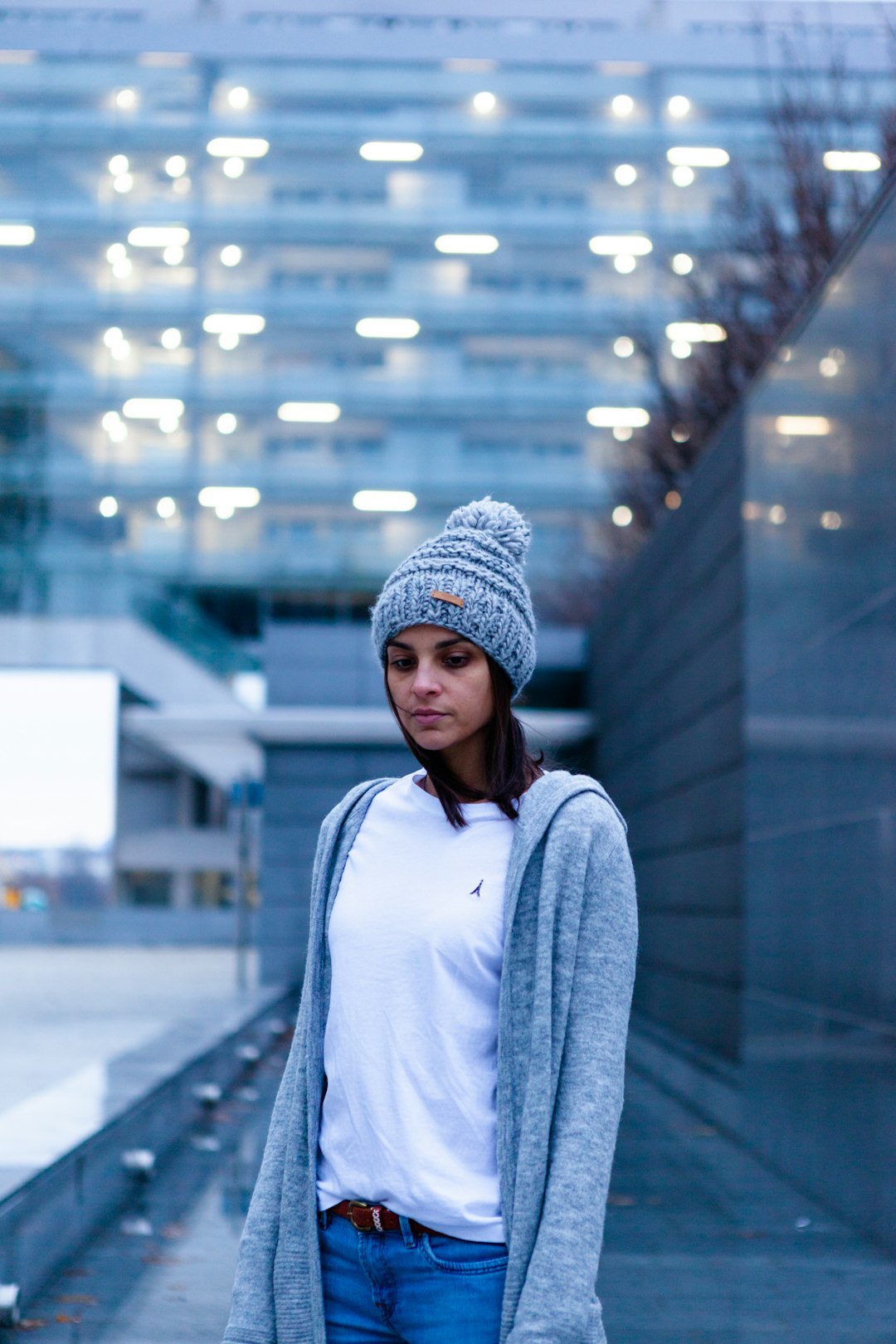 woman in gray knit cap and blue long sleeve shirt standing in front of glass building