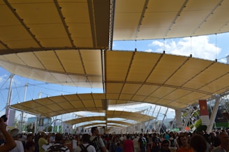 Close-up of a tensile structure canopy shading an outdoor sports facility bustling with players and spectators
