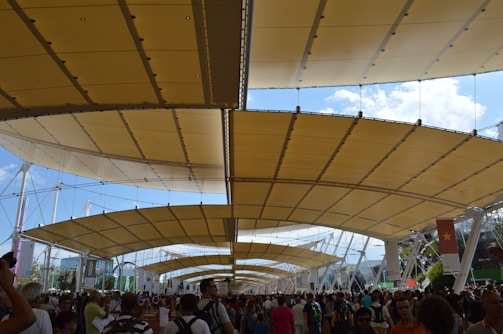 Close-up of a tensile structure canopy shading an outdoor sports facility bustling with players and spectators
