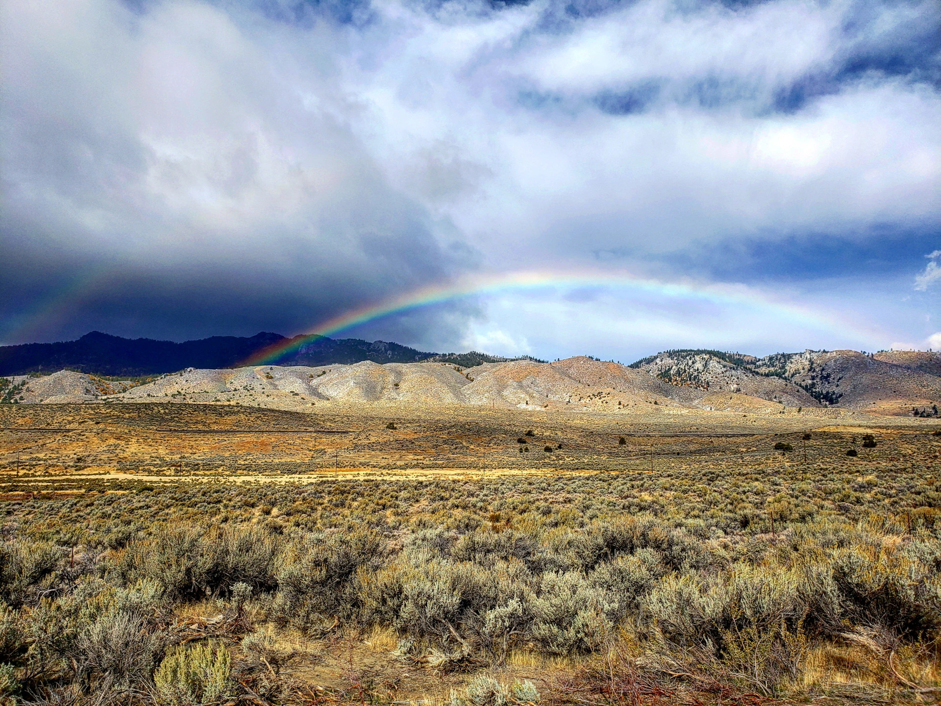 brown grass field near mountains under white clouds and blue sky during daytime