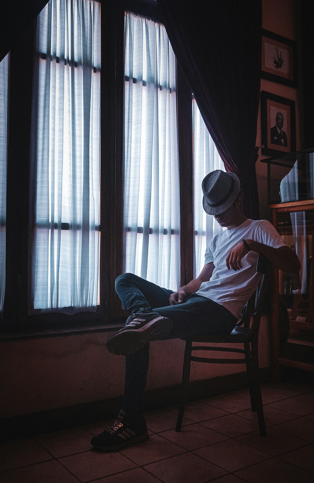 man in white shirt and blue denim jeans sitting on brown wooden chair