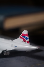 A model airplane tail fin with a distinctive red, white, and blue logo is prominently displayed. The airplane's metallic texture is evident, and the background is blurred, giving an impression of depth of field.