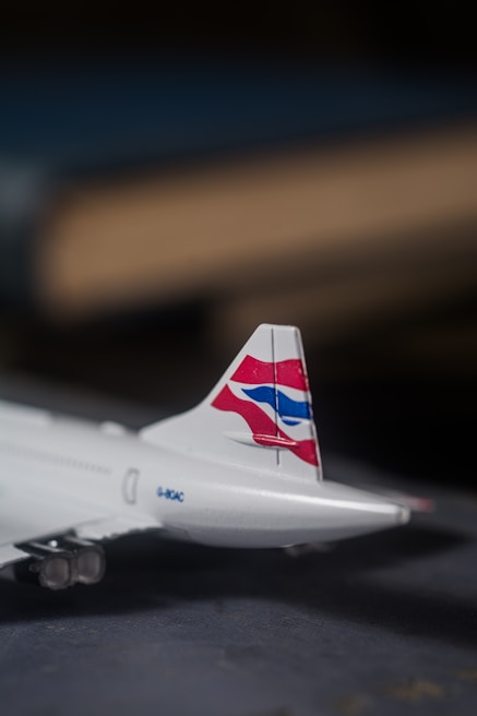 A model airplane tail fin with a distinctive red, white, and blue logo is prominently displayed. The airplane's metallic texture is evident, and the background is blurred, giving an impression of depth of field.