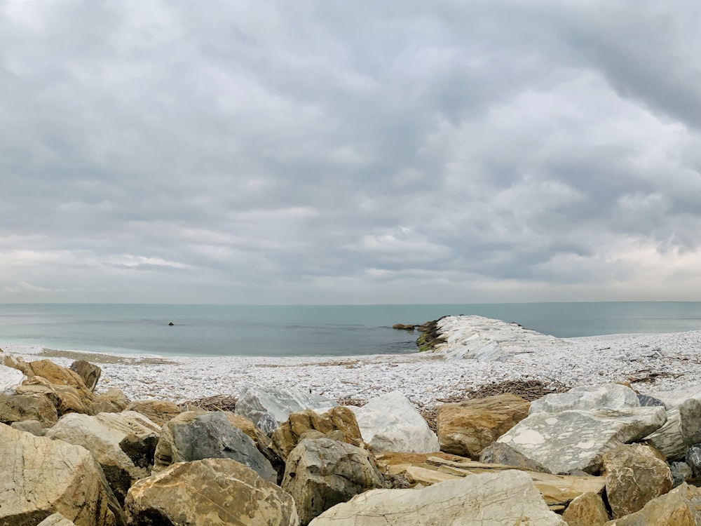 brown rocks near body of water under white clouds during daytime