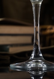 A close-up view of the stem of an elegant glass with a blurred background featuring stacked hardcover books. The focus is on the intricate details and reflective surface of the glass, creating a sophisticated and timeless ambiance.
