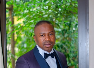 man in black suit jacket standing near green trees during daytime