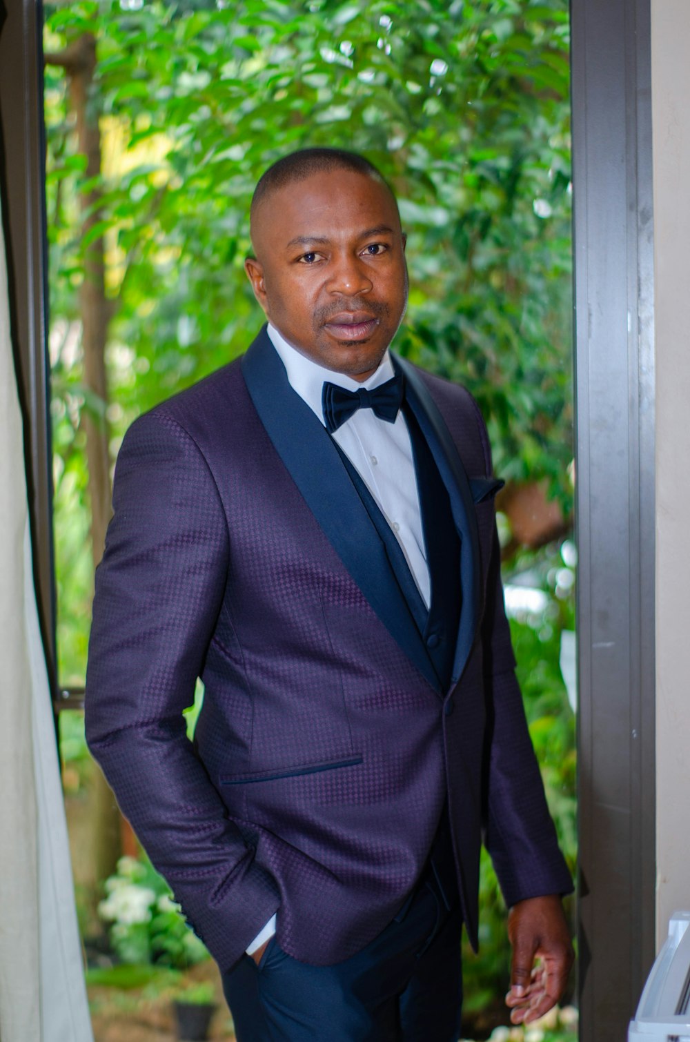 man in black suit jacket standing near green trees during daytime